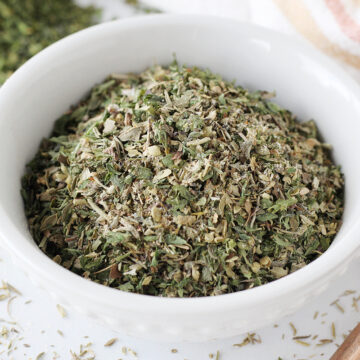 Up close photo of homemade Italian seasoning in a white bowl with a copper spoon.