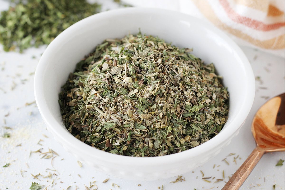 Up close photo of homemade Italian seasoning in a white bowl with a copper spoon.