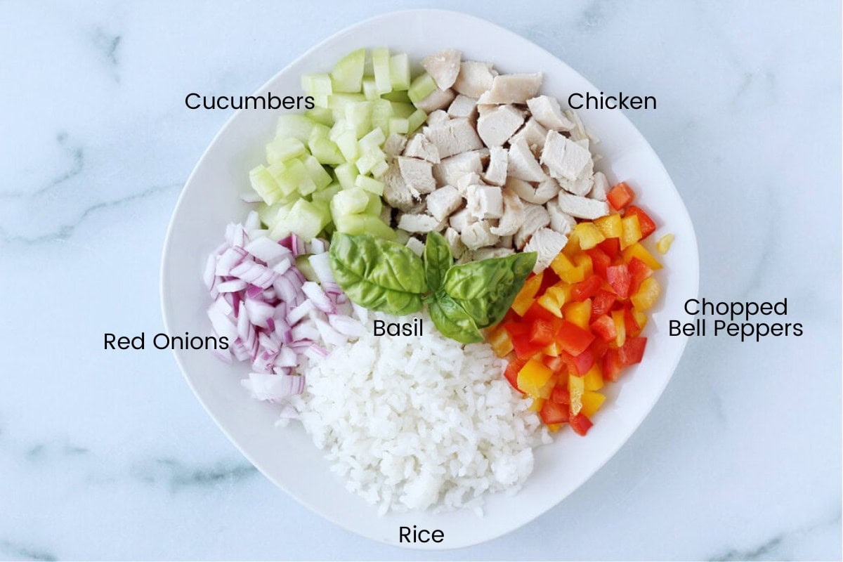 White rice, colorful bell peppers, diced chicken, cucumber and red onion in a white bowl.