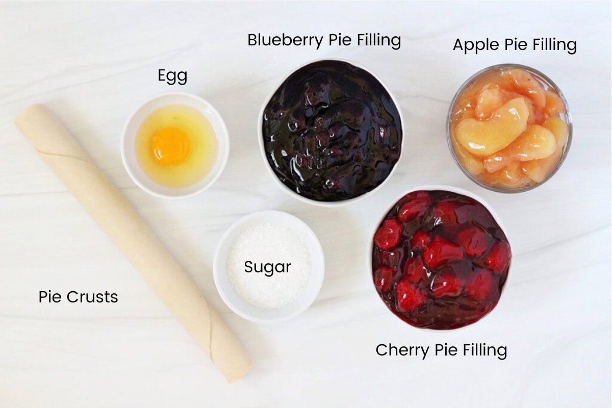 Bowls of canned pie filling, roll of refrigerated pie crust, course sugar and an egg.