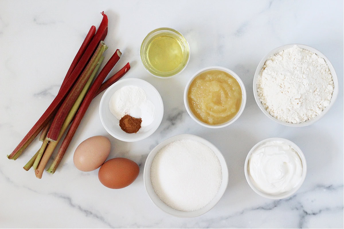 Ingredients in bowls on a white marble countertop for sour cream rhubarb muffins.