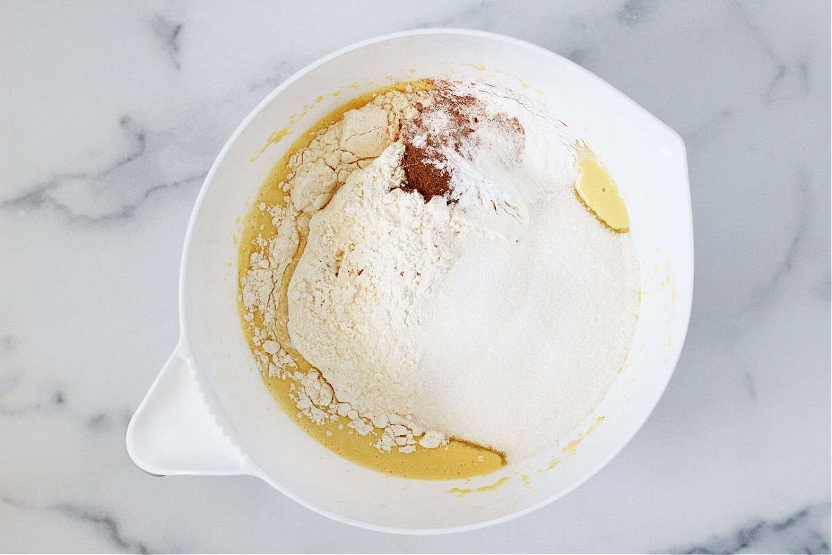 Flour, sugar, cinnamon and baking powder sitting on wet batter in a white bowl.