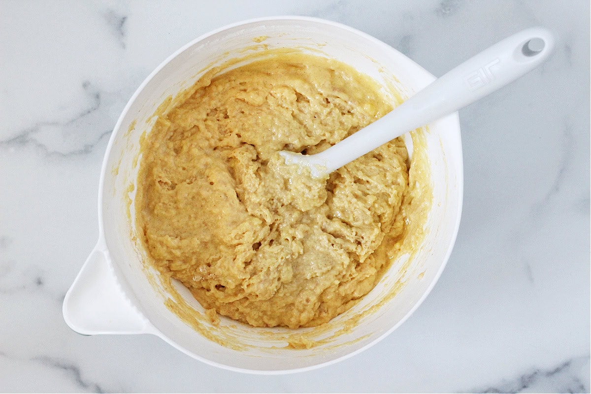 A white spatula mixing together muffin batter in a white bowl.