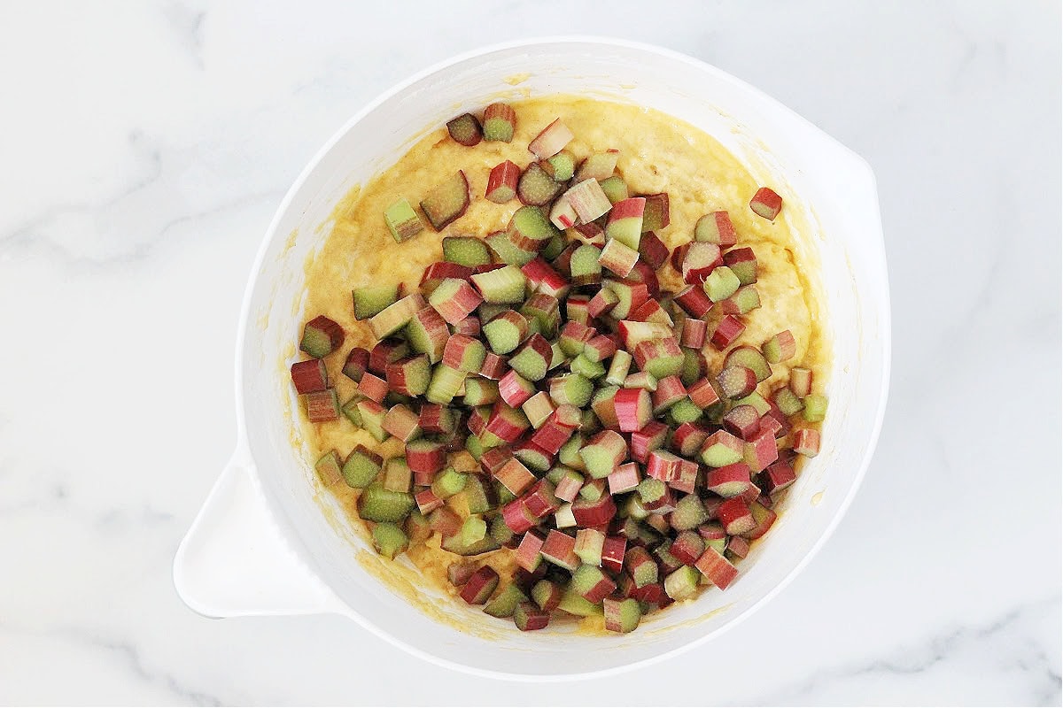 Diced rhubarb sitting on top of muffin batter in a white mixing bowl.