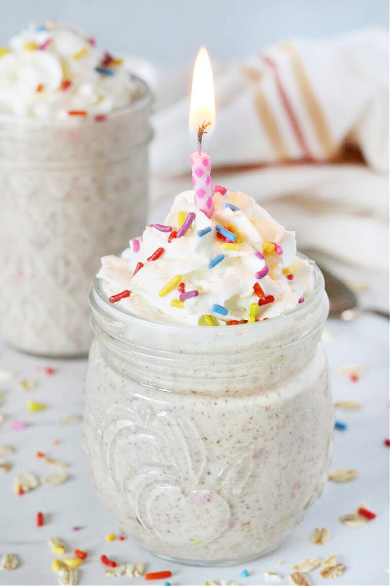 A jar of blended overnight oats topped with whipped cream, sprinkles and a birthday candle.