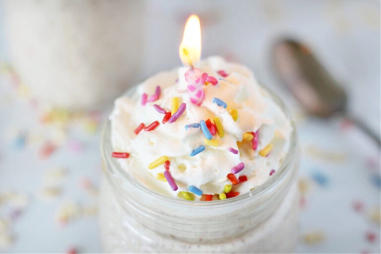 A lit candle on top of a jar of funfetti overnight oats with sprinkles.