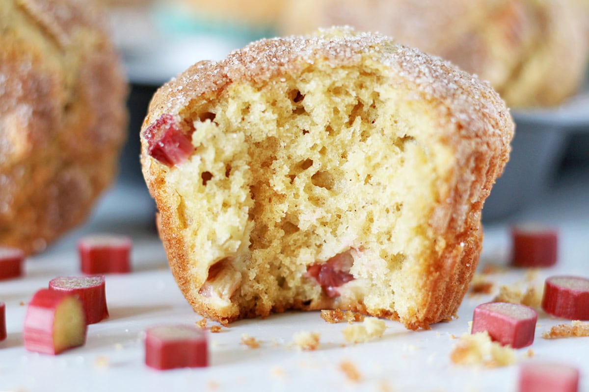 A bite taken out of a sour cream rhubarb muffin sitting on a white countertop.