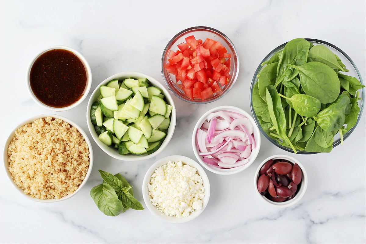 Ingredients in bowls for Greek Mason Jar Salads on a white marble countertop.