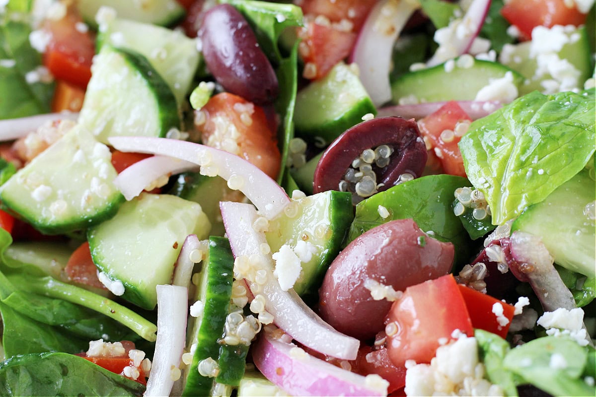 Up close photo of a salad with Kalamata olives, red onion, cucumbers and spinach.