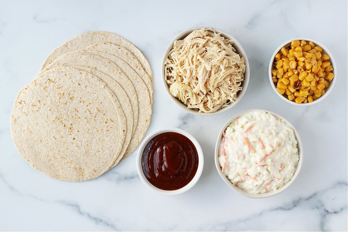 All the ingredients for BBQ chicken tacos with coleslaw, fire roasted corn and tortillas.