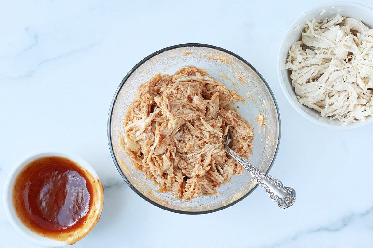 Overhead photo of three bowls - BBQ sauce, shredded chicken and BBQ shredded chicken.