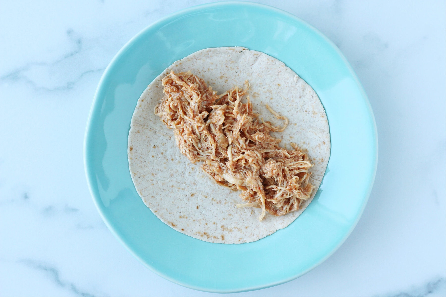 A wheat tortilla with shredded BBQ chicken on a blue plate.