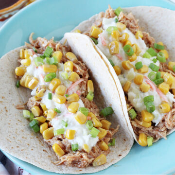 Two BBQ chicken tacos with coleslaw topped with corn on a blue plate.