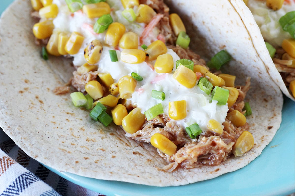 A wheat tortilla filled with shredded BBQ chicken and coleslaw on a blue plate.