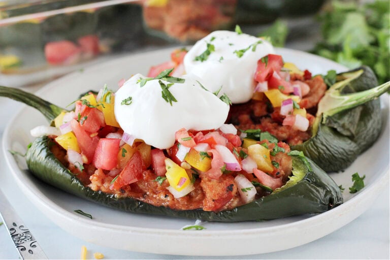 Two southwest stuffed poblano peppers on a white plate topped with sour cream and cilantro.