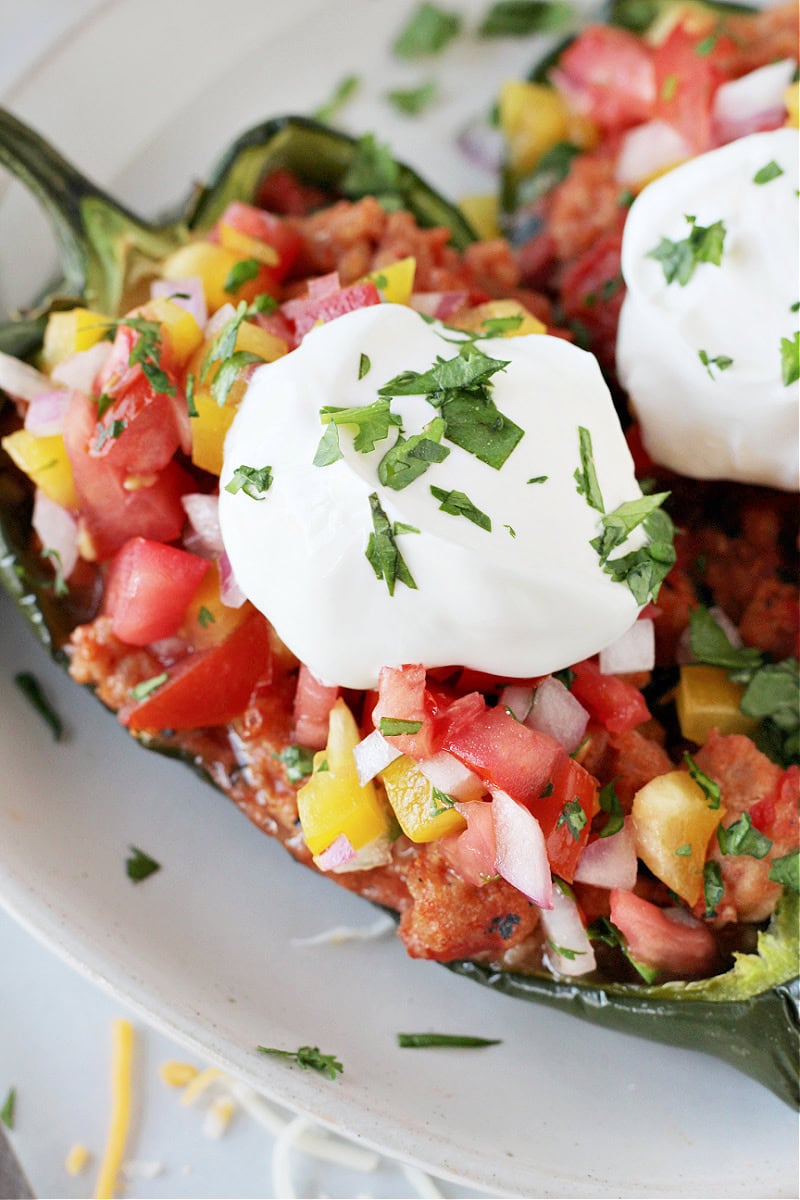 Two baked stuffed poblanos on a white plate topped with plain Greek yogurt and cilantro.