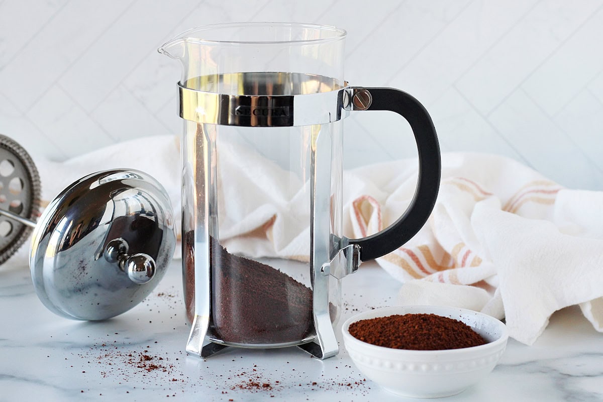 Decaf coffee grounds in the bottom of a glass French press.