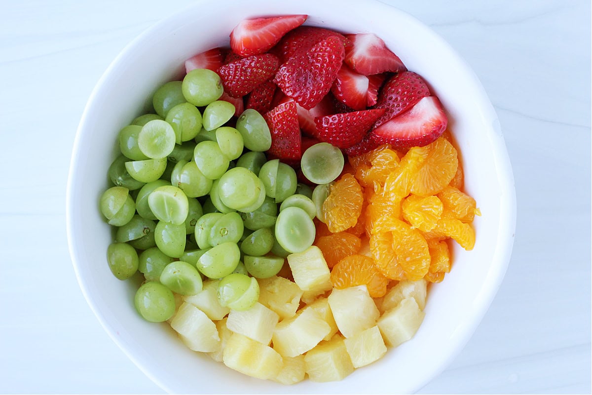 Sliced green grapes, sliced strawberries, mandarin oranges, and diced pineapple in a bowl.