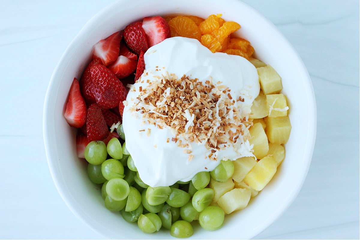 Strawberries, mandarin oranges, pineapple and green grapes with yogurt and toasted coconut shreds on top.