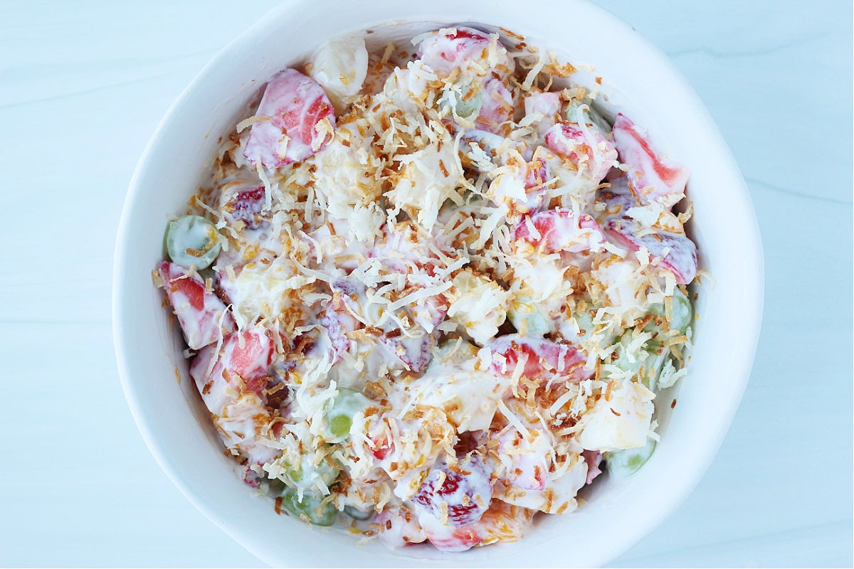 Overhead photo of summer fruits in a coconut yogurt sauce topped with toasted coconut.