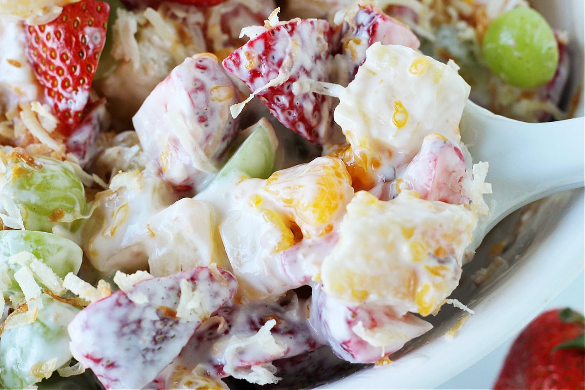 Up close photo of a white silicone spoon scooping up Hawaiian fruit salad.