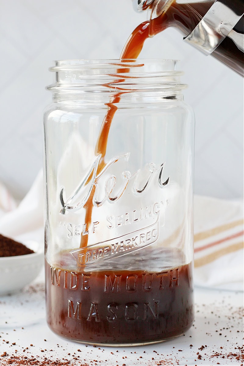 A French press pouring decaf cold brew into a mason jar.