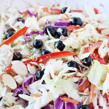 Sliced red bell peppers, blueberries and cabbage slaw in a white bowl.