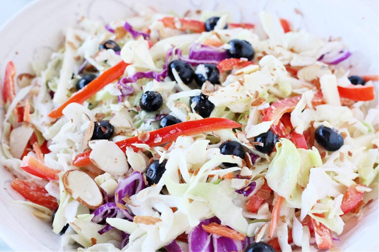 Sliced red bell peppers, blueberries and cabbage slaw in a white bowl.