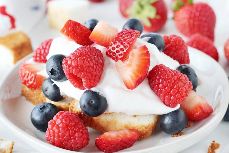 Sliced strawberries, raspberries and blueberries on whipped cream and angel food cake.