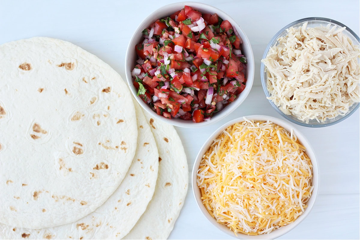 Ingredients for chicken quesadillas with homemade pico de gallo on a white countertop.