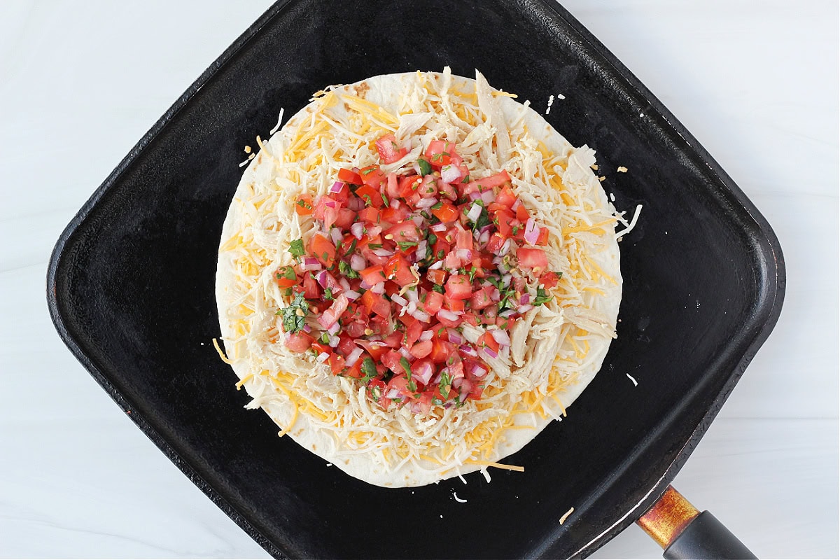 Pico de gallo on top of shredded chicken on shredded cheese on a tortilla.