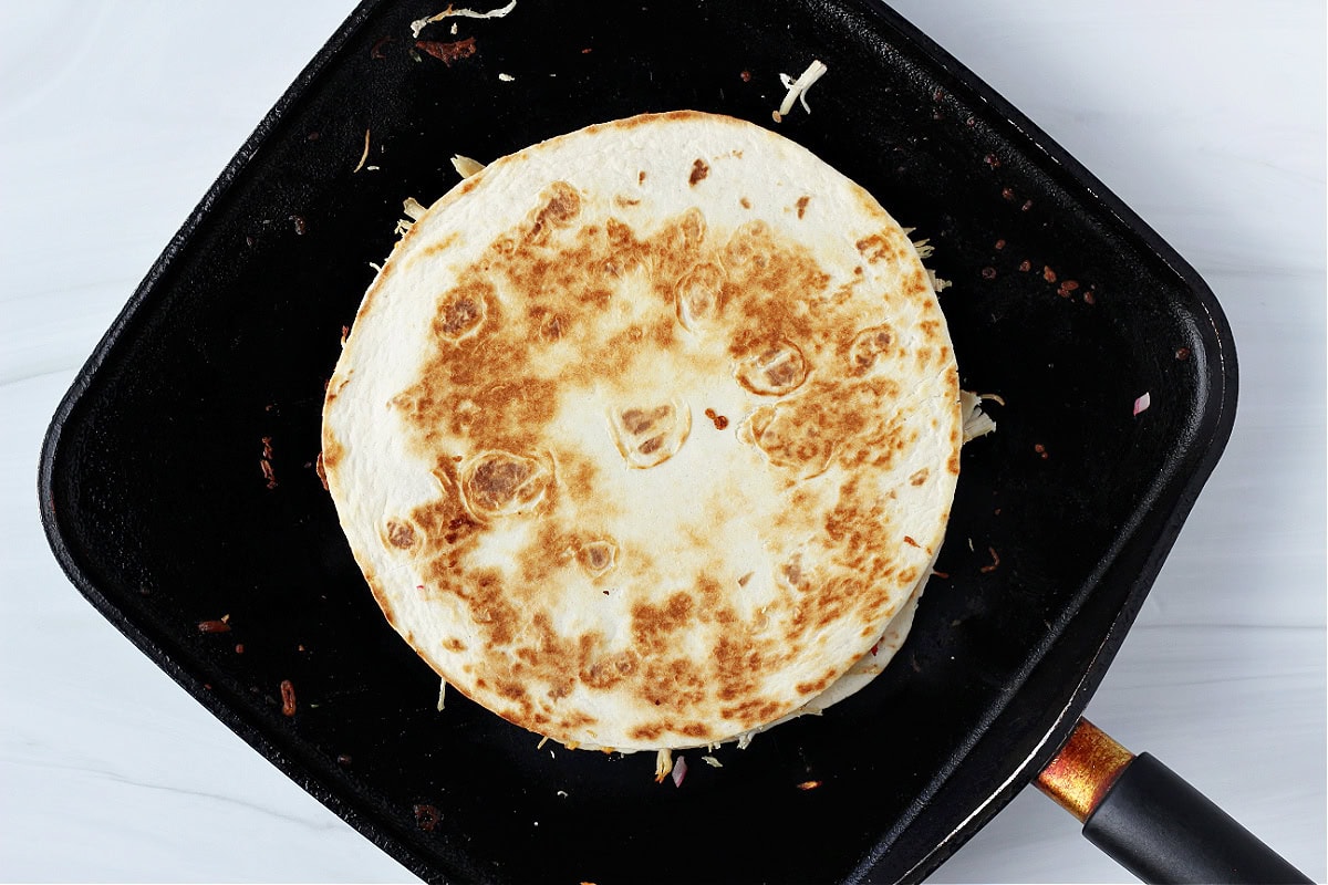 A golden brown tortilla on a chicken quesadilla on a black skillet.