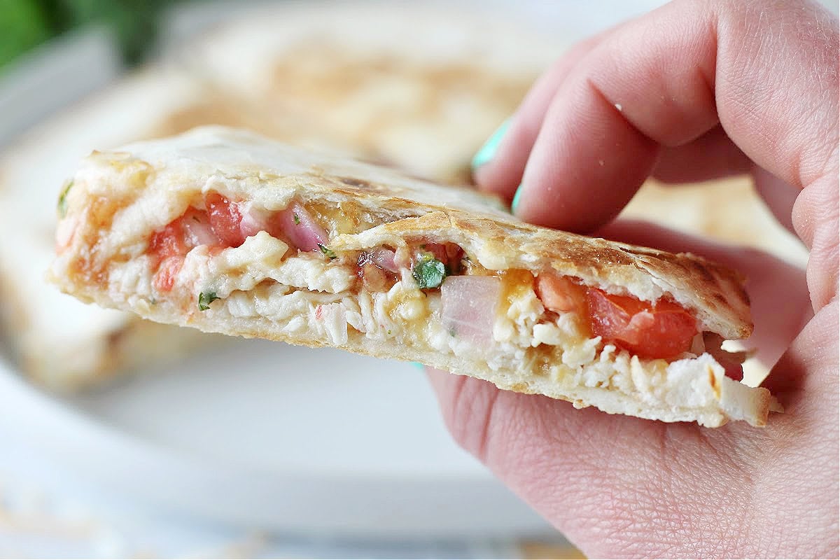 Up close photo of a slice of a quesadilla loaded with pico and chicken.