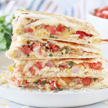 A stack of four slices of chicken quesadillas with pico on a white plate.