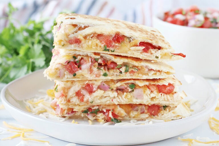 A stack of four slices of chicken quesadillas with pico on a white plate.