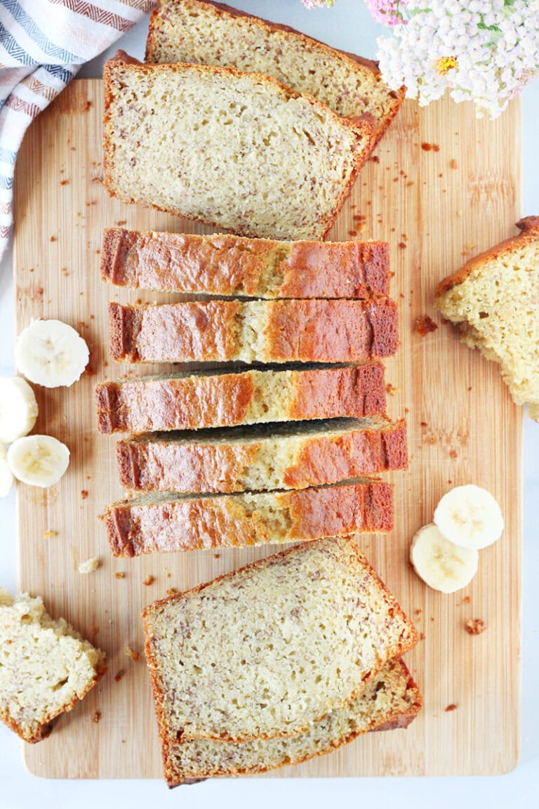 A loaf of golden banana bread cut into slices on a cutting board.