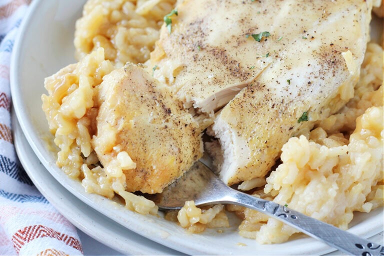 Up close photo of a fork cutting into a chicken breast over creamy rice.