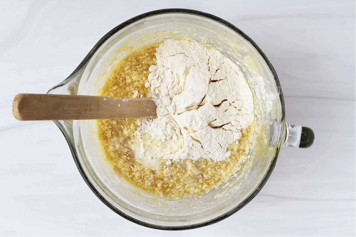 Wet ingredients in a glass bowl with the flour mixture poured on top.