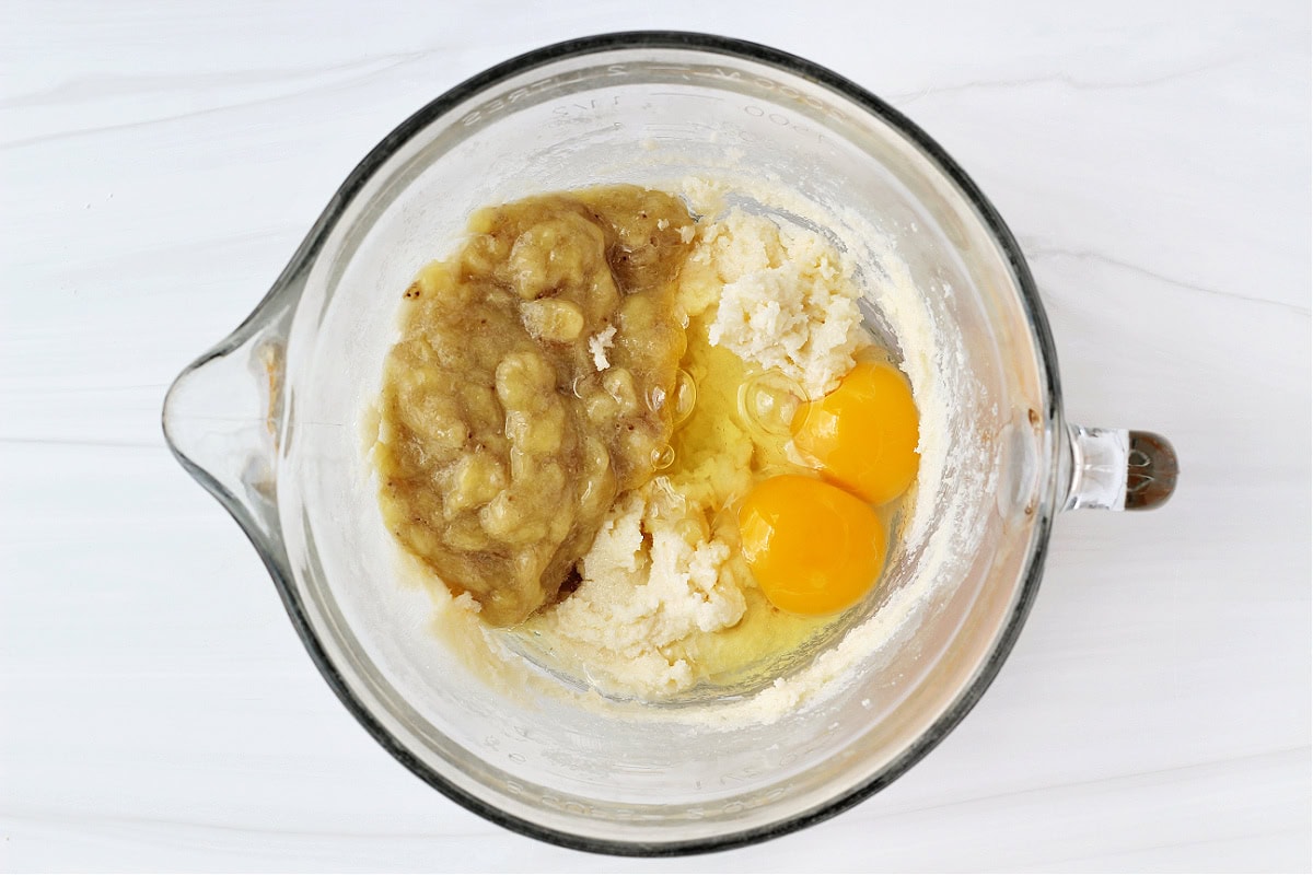 Mashed bananas, two eggs and creamed butter and sugar in a glass bowl.