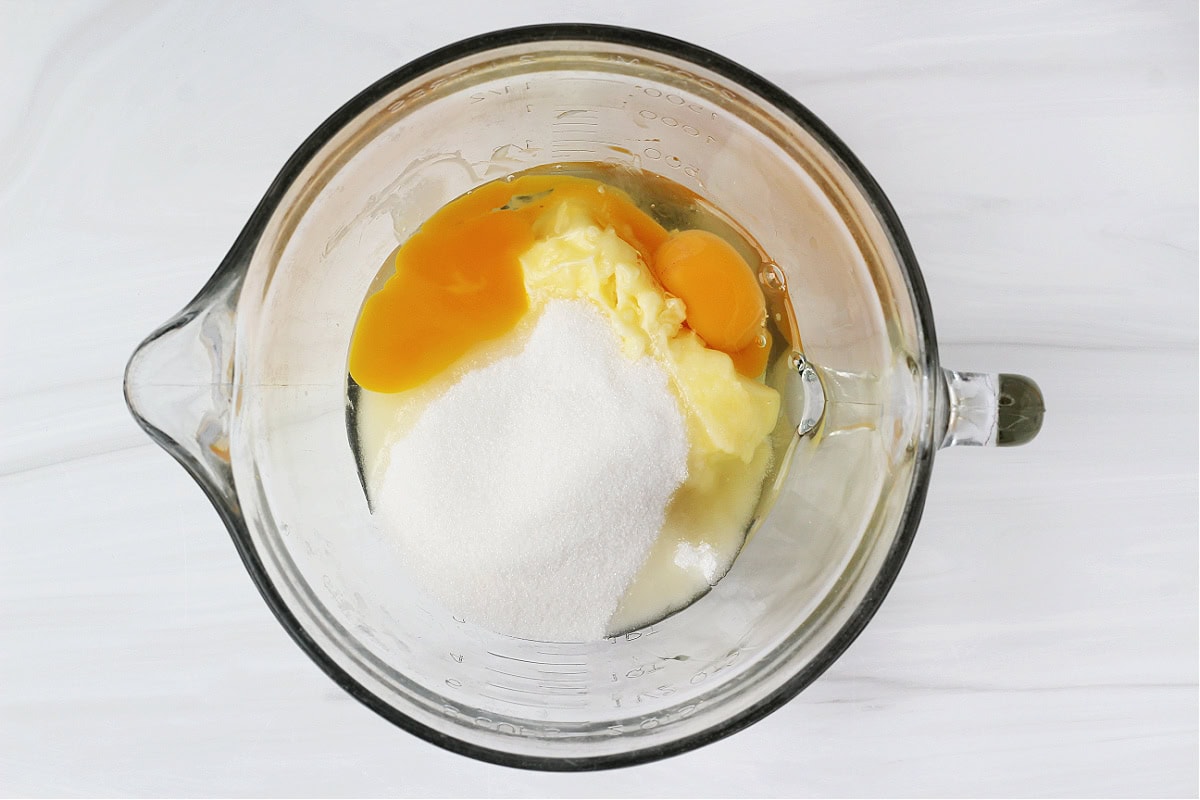 Overhead photo of butter, eggs and sugar in a glass bowl.