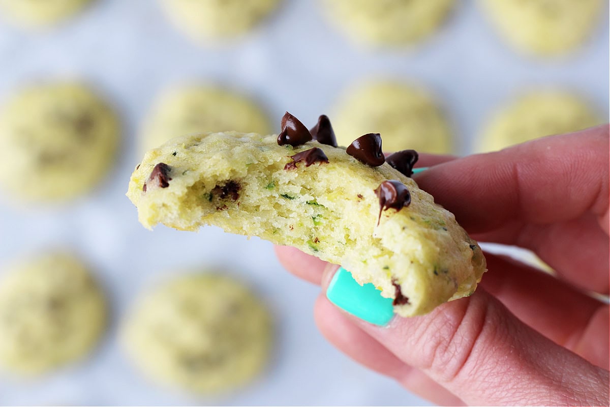 A woman's hand holding a chocolate chip coconut zucchini cookie with a bite taken out.