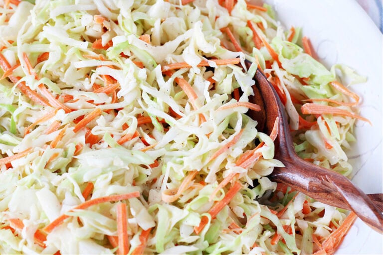 Up close photo of easy coleslaw in a white bowl with a large wooden spoon.