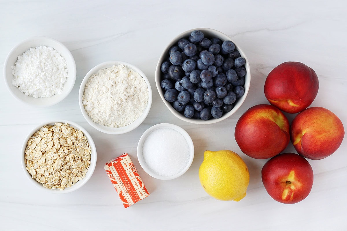 Ingredients for low sugar blueberry peach crumble on a white countertop.