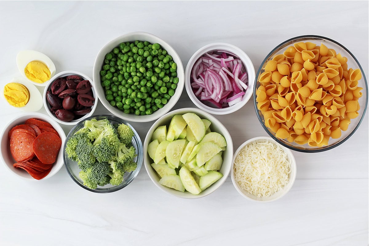 Overhead photo of loaded pasta salad ingredients in bowls.