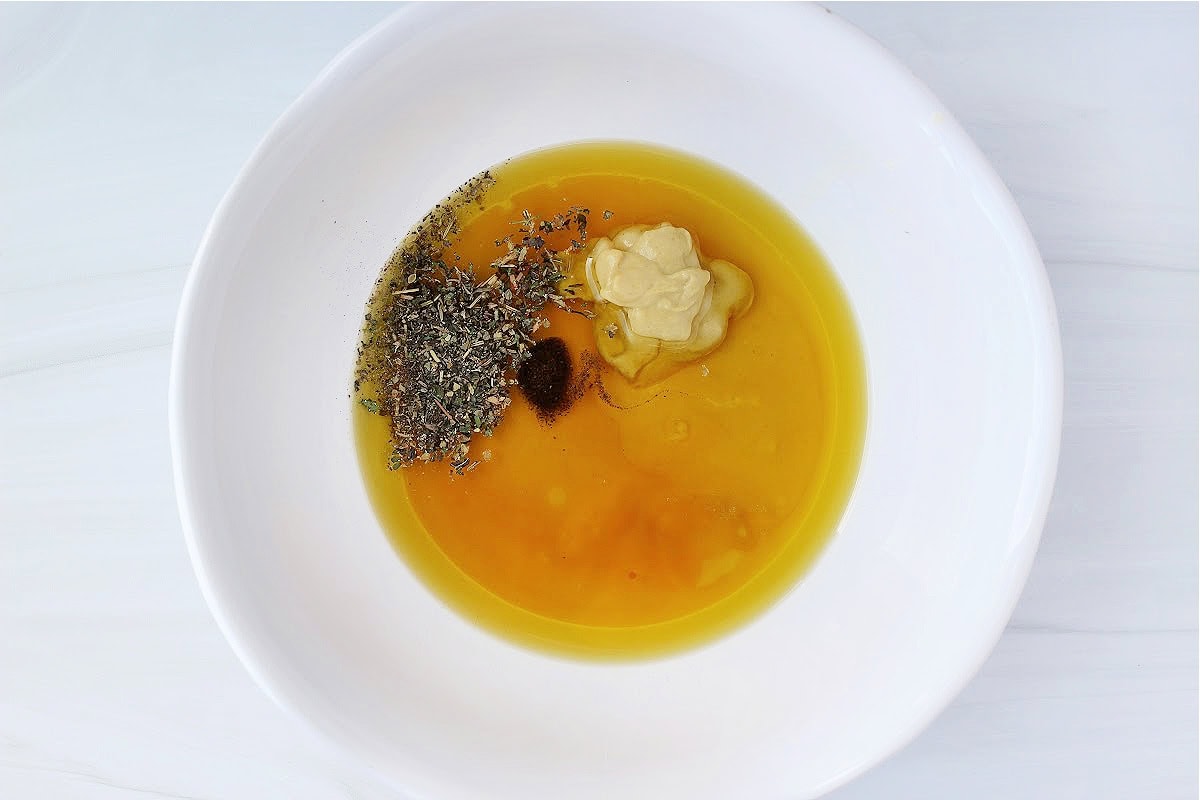 Overhead photo of olive oil, lemon juice, Dijon mustard and seasonings in a bowl.