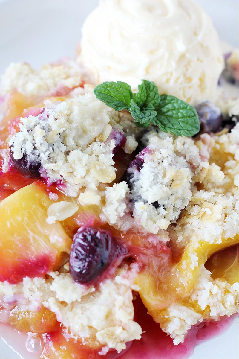 A scoop of vanilla ice cream and fresh mint leaves topping blueberry peach crumble. 