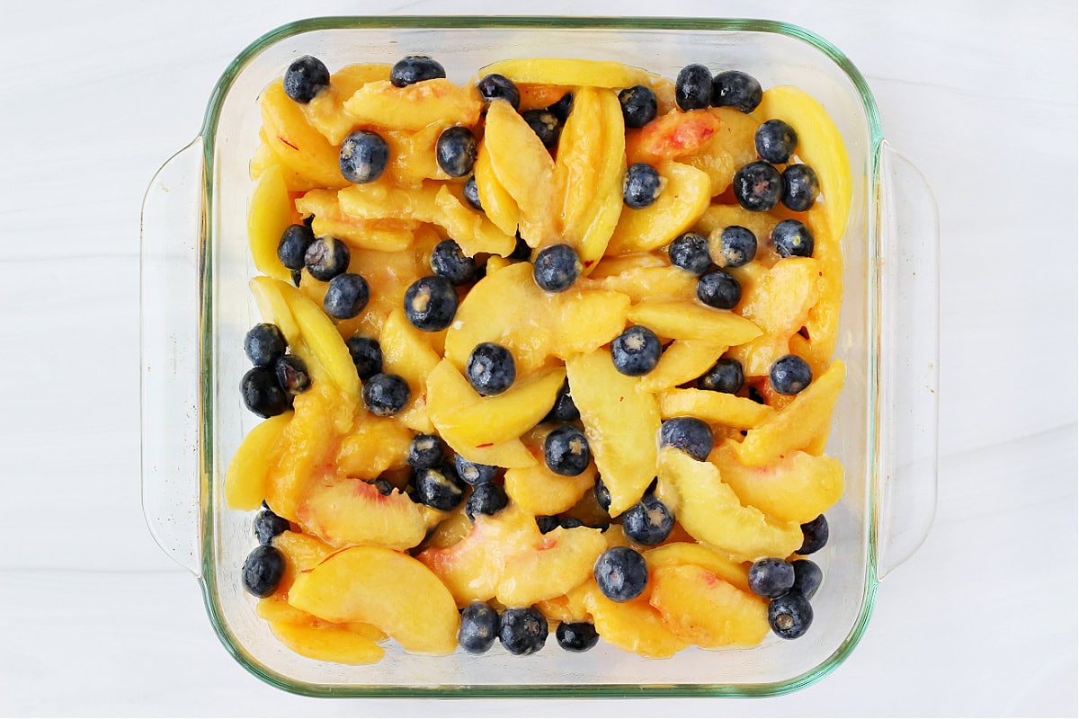 Overhead photo of a peach blueberry mixture in an 8x8 glass pan.