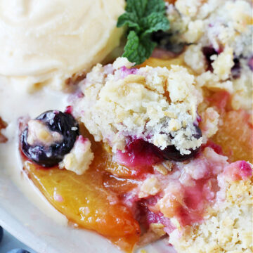 Peach crumble with blueberries topped with a scoop of vanilla ice cream.