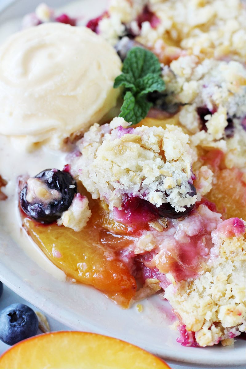 Peach crumble with blueberries topped with a scoop of vanilla ice cream.