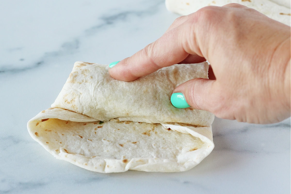 A woman's hands rolling a vegan egg roll on a marble countertop.